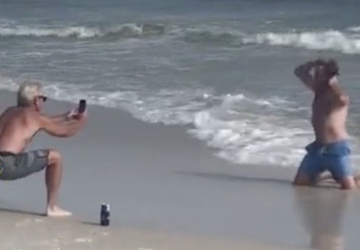 Sur une plage, deux hommes se moquent de deux filles qui prennent des photos
